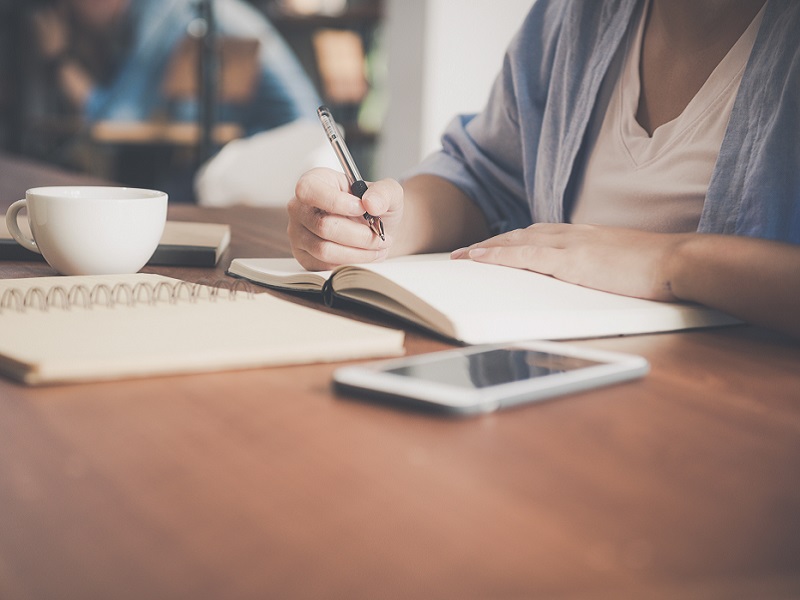 woman-writing-on-a-notebook-beside-teacup-and-tablet-733856